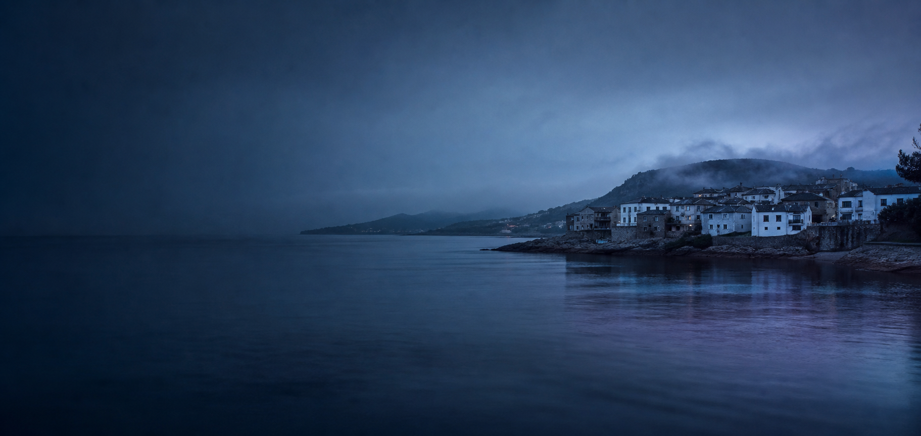 Costa de las Rías Baixas al anochecer: agua atlántica y casas blancas junto a la orilla.